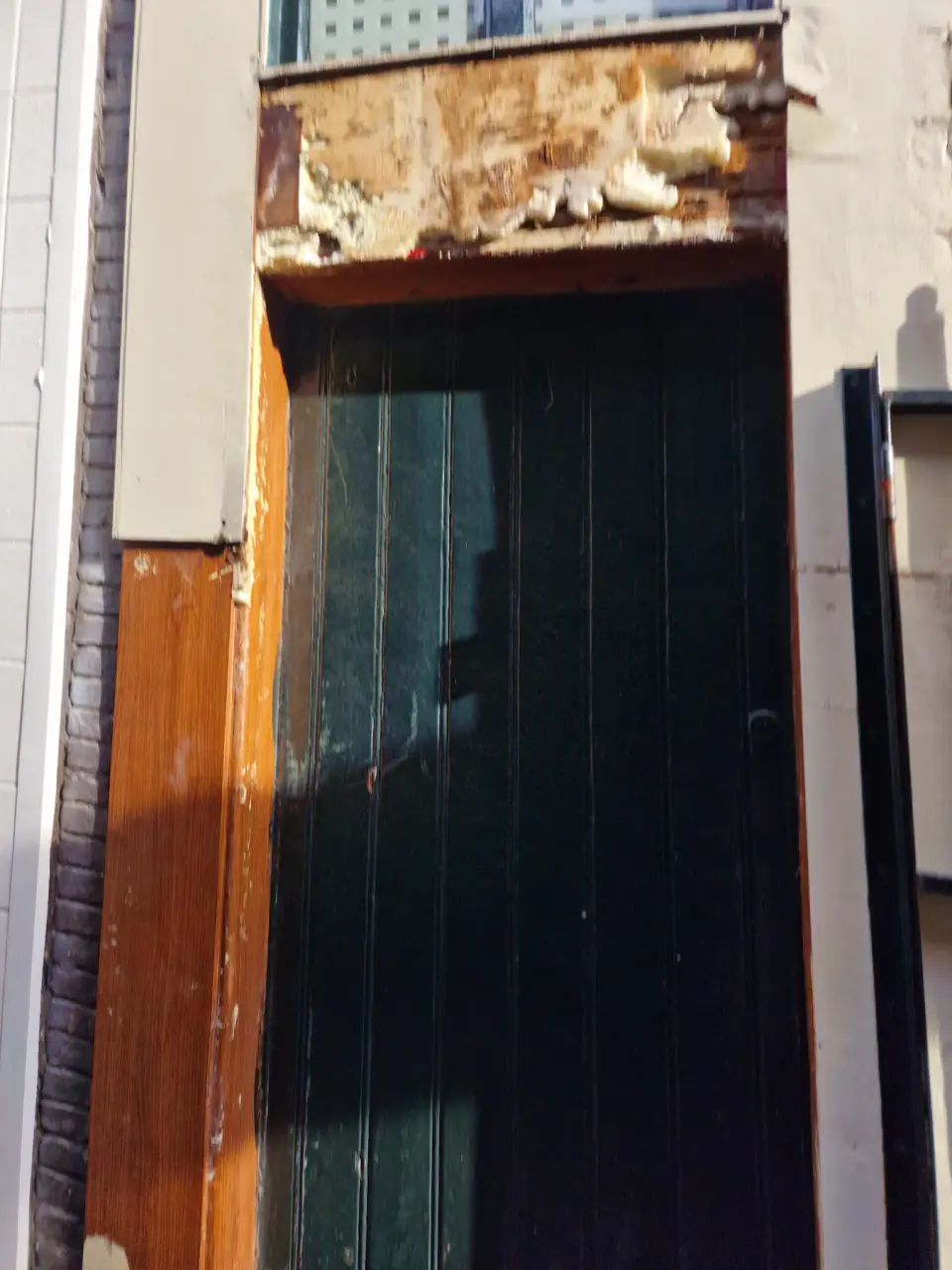 Verwijderde gevelbekleding boven een deur tijdens de houtrenovatie